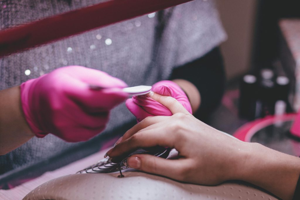 Manicure con smalto rosa eseguita con guanti professionali